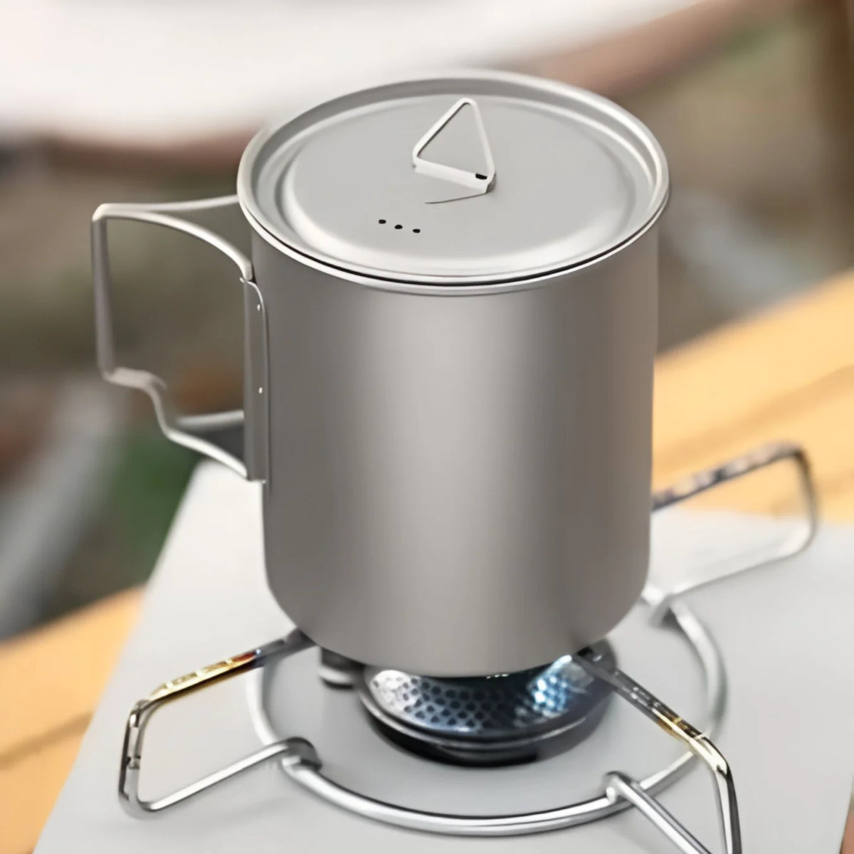 Silver camping mug with a lid on a small stove